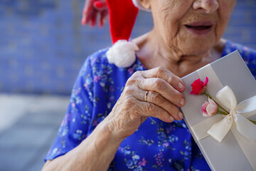 old woman with santa hat opening a christmas present in xmas. Happy elderly in christmas