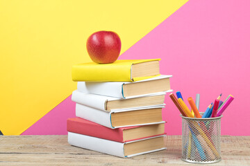 Books stacking. Books on wooden table and pink, yellow background. Back to school. Copy space for ad text.
