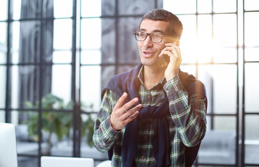 Handsome man talking on smartphone in front of office window