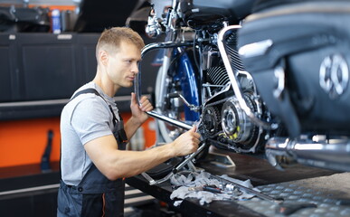 Male car mechanic holds wrench and looks at open motorcycle engine. High-quality motorcycle repair...