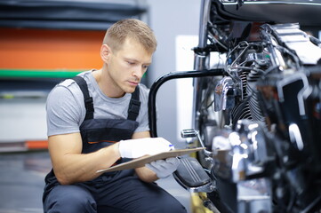 Fototapeta na wymiar Young car mechanic conducts diagnostics of motorcycle engine in car service. Car and motorcycle warranty service concept