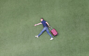 Young man with suitcase walking on green grass top view. Travel dreams concept