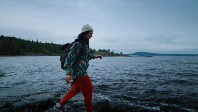 Active Pastime In Weekend, Woman With Backpack Walking On Stone Shore Of Beautiful Lake