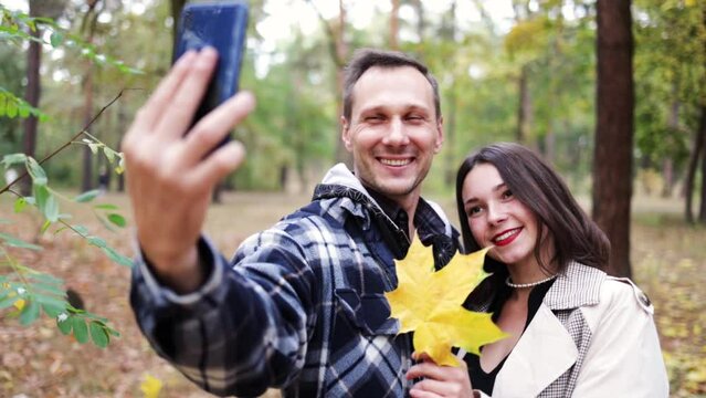 Attractive young couple spending time together taking selfie by smartphone in autumn park.  