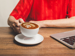 Close-up of a senior woman holding a white coffee cup while sitting at the table.