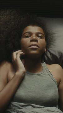 Vertical top down shot of black teenage girl lying in her bed and rubbing eyes having having depression and crying