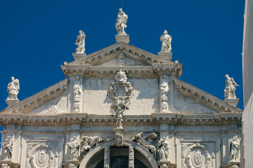 Architectural elements of a snow-white Catholic cathedral against a blue sky in Venice, Italy.