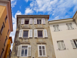Old three-story colorful houses with windows with shutters and blue sky with clouds.