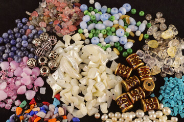 A variety of beads made of natural stone, glass, mother-of-pearl, ceramics and metal on a black...