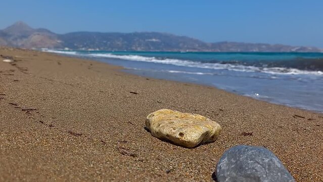 Ripresa video a livello terreno di una spiaggia di sabbia con una pietra che viene sommersa da un'onda