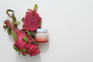 Cosmetic jar without label decorated with red dragon fruit over light background. Dragon fruit (Hylocereus) is a tropical fruit that is nutrient-rich. Blank space for advertising.