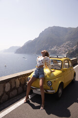 beautiful woman with blond hair in elegant fashion clothes posing near a yellow retro car on the Amalfi coast in Positano