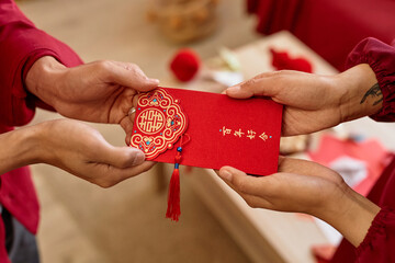 Close up of two people handing ornate red envelope as Chinese New Year tradition for good luck Have...