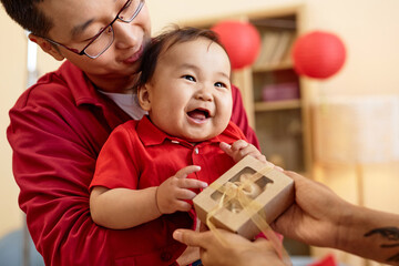 Portrait of cute Asian baby holding box of fortune cookies with family celebrating Chinese New Year...