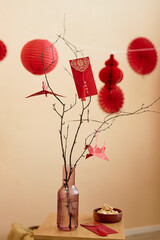 Minimal background image of tree branches decorated with paper cranes and red envelopes as Chinese...