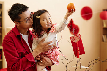 Waist up portrait of happy Asian girl holding tangerine while celebrating Chinese New year with...