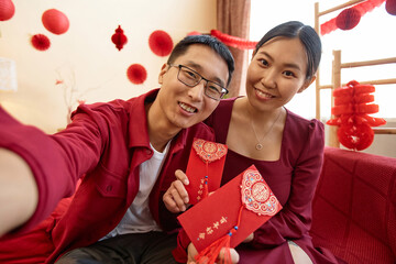 POV of young Asian couple wearing red on Chinese new year and taking selfie photo together at home...