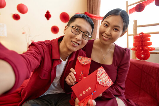 POV of young Asian couple wearing red on Chinese new year and taking selfie photo together at home Have overflowing abundance every year