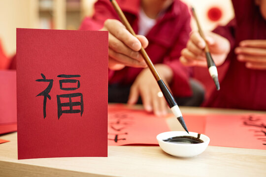 Closeup of Asioan family doing traditional calligraphy together with focus on hand drawn Fu character on red, copy space Happiness inscription
