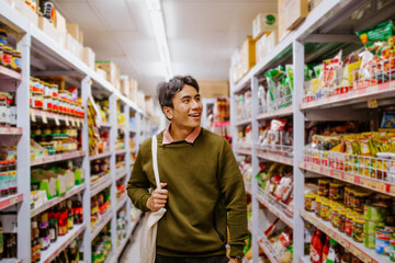 Man holding tote bag walking down supermarket aisle