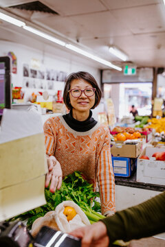 Woman gesturing to payment terminal at supermarket counter