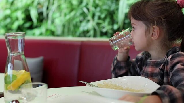 A charming girl 5-6 years old drinking water in cafe while having a dinner