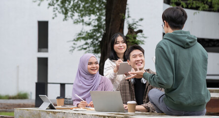 Multiracial smiling group of teenage student using laptop doing homework and enjoying a relaxed atmosphere outdoors at the university campus. Education concept. High quality photo
