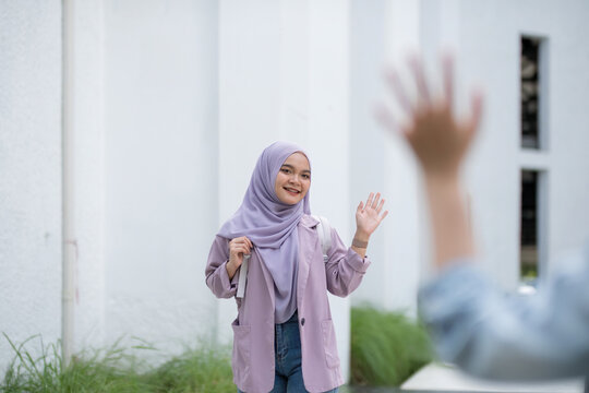 Beautiful Muslim college student girl waving to greet a friend at university