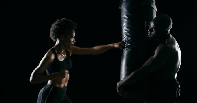 Woman, coaching and punching bag with fitness, workout and training for MMA or gym boxing in studio. African boxer and personal trainer helping with sports, fight or power on dark or black background