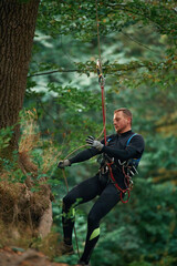 Naklejka na ściany i meble Activity, hanging on a rope. Man is doing climbing in the forest by use of safety equipment