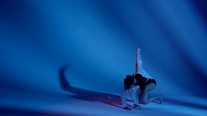 Young woman wearing a top, shorts and a shirt performing contemporary dance in studio. Neon blue...
