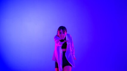 Young woman wearing a top, shorts and a shirt performing contemporary dance in studio. Neon blue, pink and red color scheme, ombre, gradient background. Medium sized.