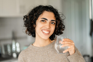 Portrait happy curly middle eastern woman looking at camera and drinking water