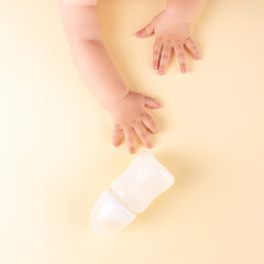 The baby's hands reach for the milk bottle on a yellow background. Concept, top view, copy space.