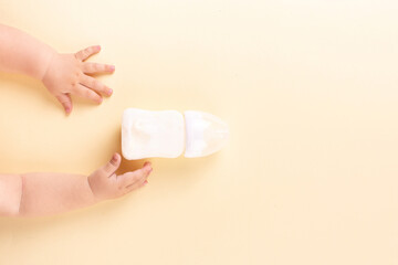 The baby's hands reach for the milk bottle on a yellow background. Concept, top view, copy space.