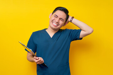 Stressed professional young Asian male doctor or nurse wearing a blue uniform holding clipboard and...