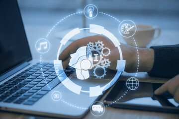 Close up of male hands using laptop and tablet on desk with creative glowing round head outline ai hologram on blurry background. Machine learning, artificial intelligence concept. Double exposure.