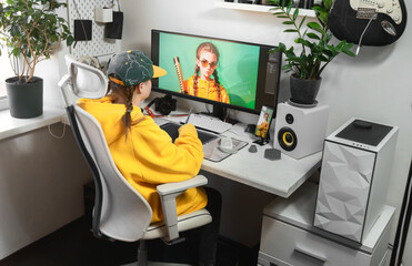 A young girl draws on a PC using a graphics tablet in comfortable home office.
