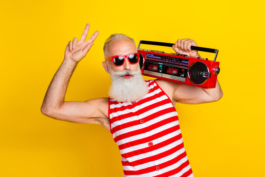 Photo of cool grandfather wearing striped overalls show v sign listening vintage cassette player isolated on yellow color background