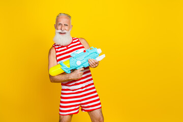 Photo of brutal crazy grandfather red striped swim shorts overalls splashing water gun at swimming pool isolated on yellow color background
