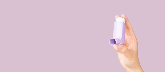 Hands holding asthma inhaler on purple background. Pharmaceutical product is used to treat lung...