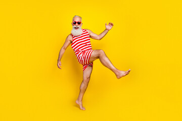 Full length photo of excited funky elderly guy dressed striped red swimsuit dancing walking isolated yellow color background