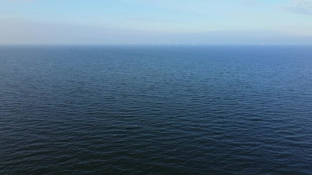 Drone flight over the sea. Calm water surface in the sea with large ships on the horizon