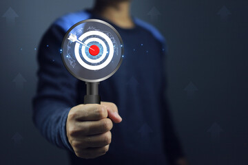 Hand holding magnifying glass with dart board represent to goal researching information and market...