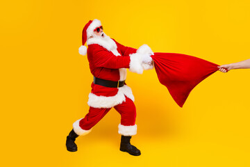 Fototapeta na wymiar Full length profile photo of grandfather santa fight new year gifts bag person arm pull isolated on yellow color background
