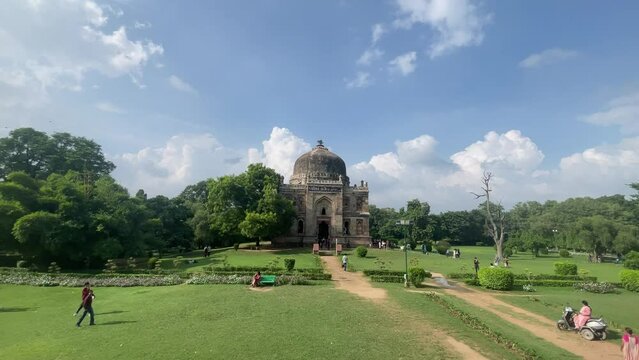 Tourists and locals walking in Lodhi Gardens with Shish Gumbad in the background in Delhi, India