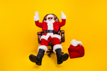 Fototapeta na wymiar Full body photo of grandfather wear red santa claus costume arms up sit armchair happy new year party isolated on yellow color background