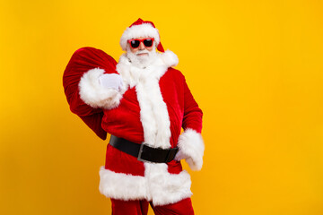 Photo of cheerful eccentric aged santa hold christmas festive presents bag empty space isolated on yellow color background