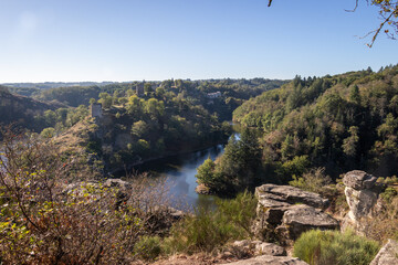 An early morning view (Rocher de la Fileuse) of Medieval ruins of fort at Crozant in Creuse, France. A view across the valley and river confluence of the Sedelle with rocks in the foreground.
