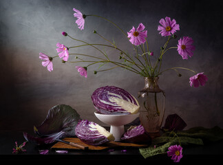 Modern still life with cut red cabbage and pink flowers in a vase on a dark table